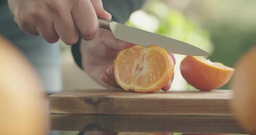 Person Slices Orange on Cutting Board Outdoors