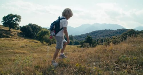 Boy Hikes Through Sunny Grassy Hillside