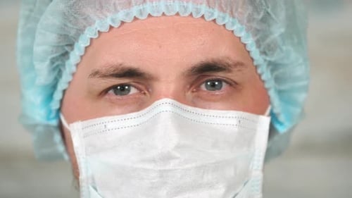 Gesicht eines Mannes mit Haube und weißer medizinischer Schutzmaske