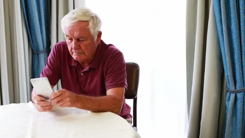 Senior Man Using Smartphone at Table Indoors