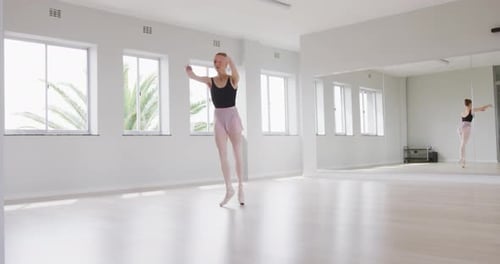 Caucasian female ballet dancer practicing ballet during a dance class in a bright studio