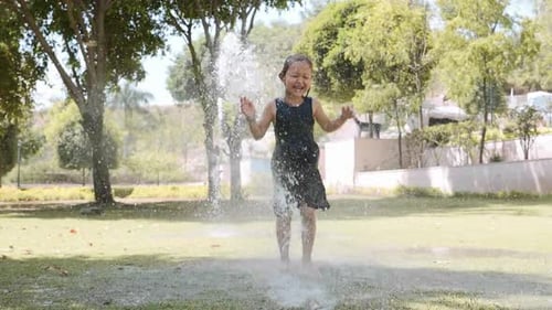 Happy Girl is Jumping in Puddle Under the Water Jet in Park