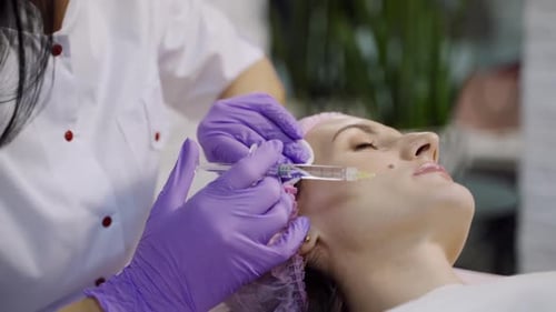 Eine erfahrene Kosmetikerin führt Mesotherapie für eine Frau durch, die auf einer Couch liegt