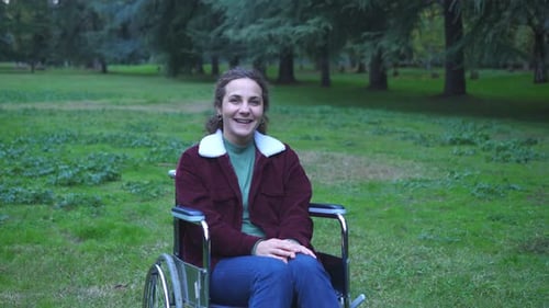 young woman using wheelchair alone in the park smiles at camera