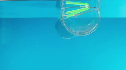 Schwimmendes Plastikglas mit einer Cocktailröhre im Meer, die Müll in den Fluss oder See wirft