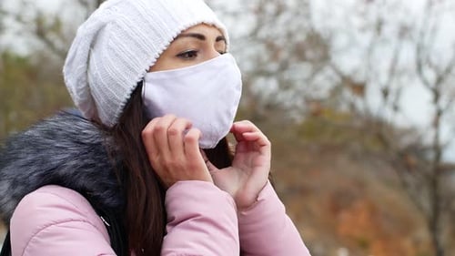 A woman with long dark hair in a mask from air pollution and the Covid19 coronavirus walk