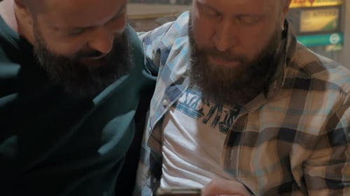 Close up view of two white mature bearded men using smartphone together
