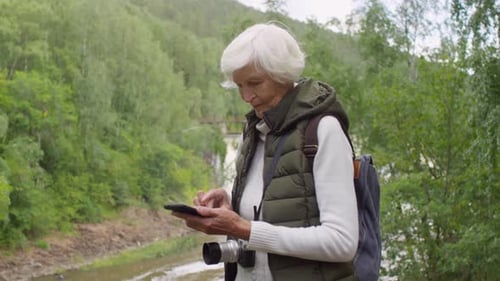 Active Senior Woman Using Phone by River