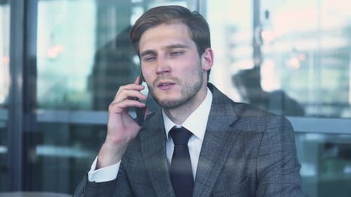 Young Businessman in a Suit Is Sitting on the Terrace of a Cafe and Working on a Laptop, Talking