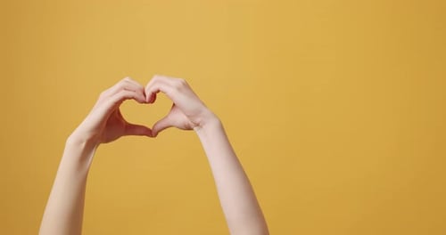 Hands Making Heart Shape on Yellow Background