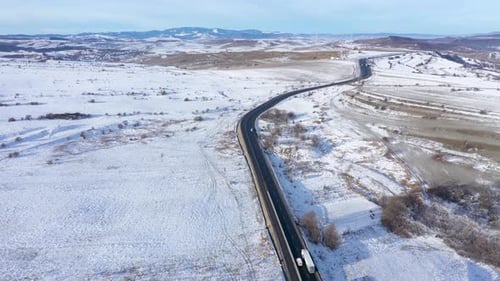 Luftaufnahme einer kurvenreichen Straße mit fahrenden Autos an einem frostigen sonnigen Wintertag