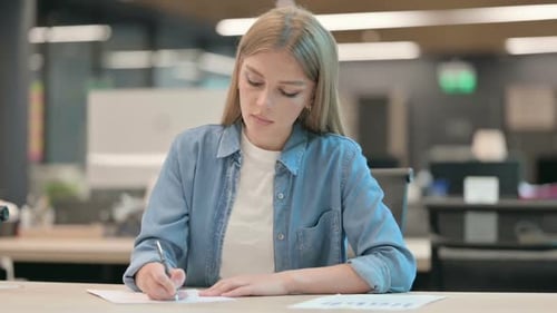 Young Woman Writing on Paper in Office