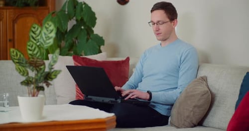 Young Adult Typing on Laptop on Couch at Home