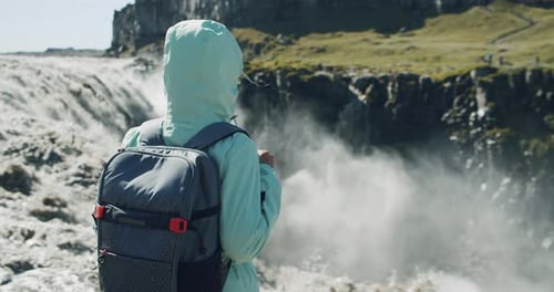 Rückansicht einer Frau, die am Rand der Klippe steht und auf den Detifoss-Wasserfall in Island blickt