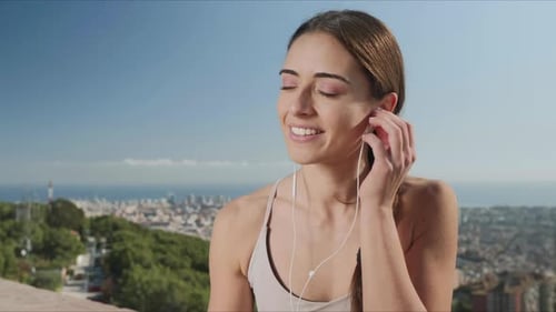 Woman Putting on Earphones in City of Barcelona. Girl Listening Music in Earbuds