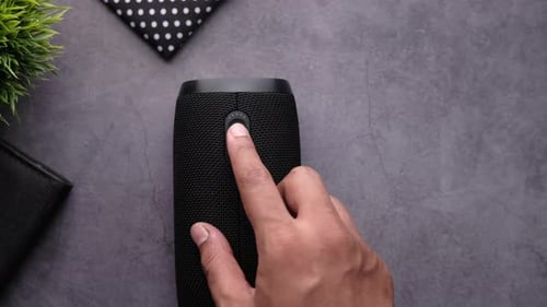 Hand Turning On Wireless Speaker on Table