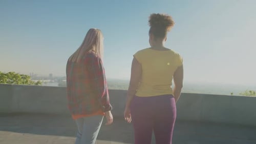 Women Holding Hands Admire Skyline View on Rooftop