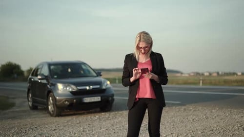 Pretty Blonde Calls and Talks on a Smartphone at a Broken Car Near the Highway