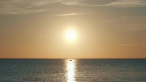 Lonely boat sits at sea during sunset in sun's reflection, long shot