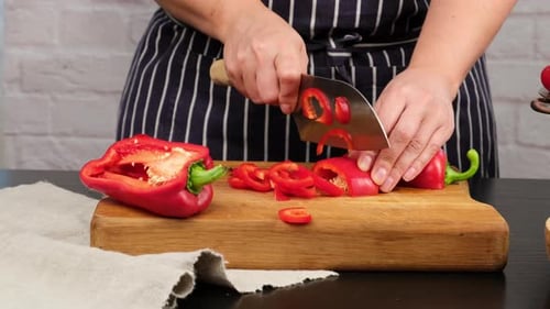 Hands Cutting Fresh Red Pepper on Wood Board
