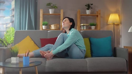 Woman Massaging Foot on Couch at Home