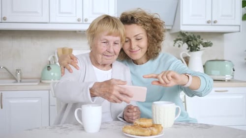 Two Women Looking at Cellphone Together in Kitchen