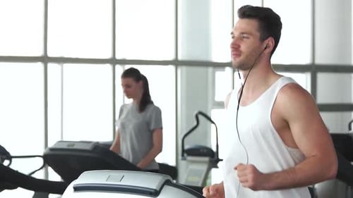Man and Woman Jogging on Treadmills at the Gym