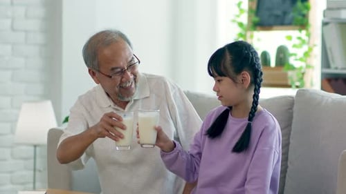 Grandfather and Granddaughter Drink Milk Together Indoors