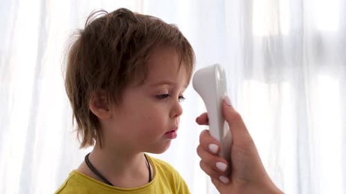Woman Measures Boy Temperature with Noncontact Thermometer