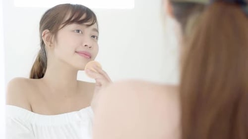 Woman Applying Makeup with Sponge in Bright Mirror