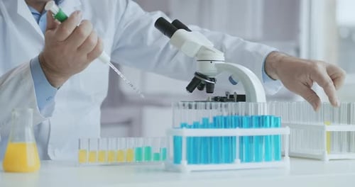 Scientist Using Pipette and Looking Through Microscope