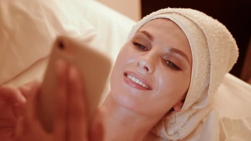 Woman Smiles Using Smartphone in Bed with Towel