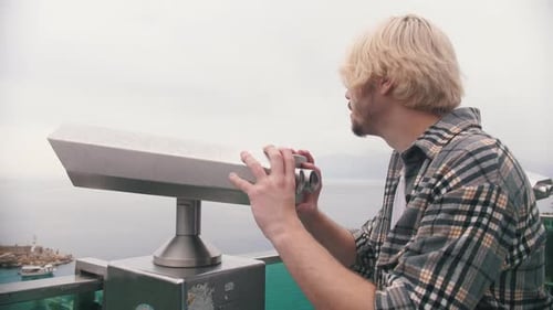 Blonder Mann in einem karierten Hemd blickt von der Aussichtsplattform aus durch das Teleskop