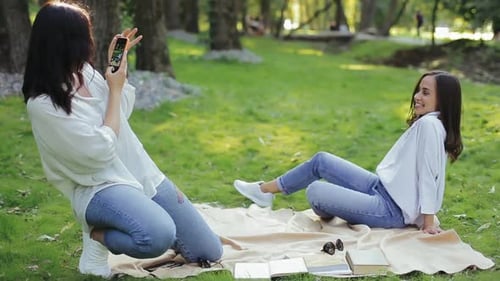Mädchen fotografiert ihre Freundin im City Sunny Park im Frühjahr auf dem Smartphone. Zwei lächelnde Freundinnen