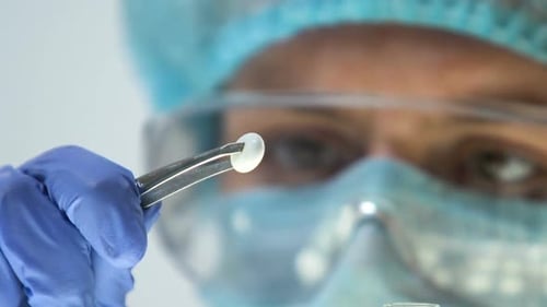 Surgeon Holding Small Round Implant with Tweezers