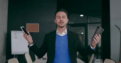 Young Serious Businessman Working in the Office Meditating in the Workplace with Closed Eyes