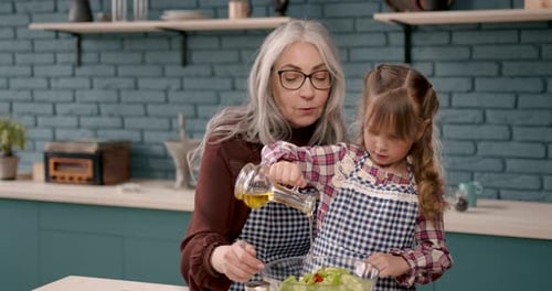 Gray Haired Woman Helping Girl Prepare Salad in Kitchen