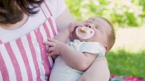 Mother with a Newborn Baby Walks in the Park. Young Mother Holds Her Baby in Her Arms. Breast
