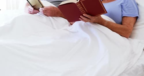 Loving Elderly Couple Reading Books in Bed