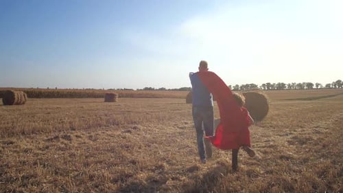 Adult and Child Running in Field Wearing Red Capes
