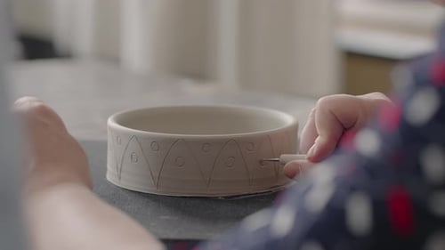 Person Decorating Ceramic Bowl with Tool