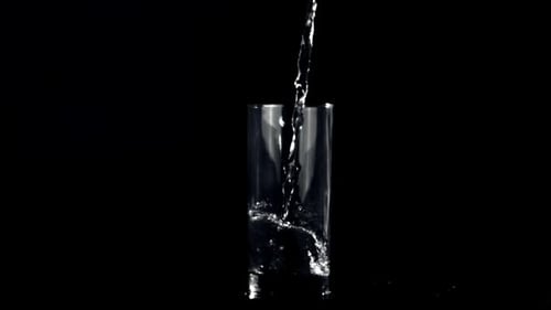 Water Pours into Glass in Dark Setting