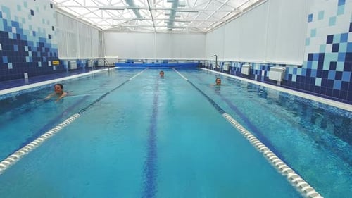 Two Smiling Women and a Young Man Swimming in Different Pool Lanes