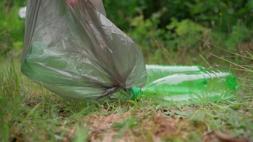 Un trabajador de limpieza retira la basura y la basura en una bolsa en la pradera del bosque. Día soleado. Cámara lenta. Primer plano