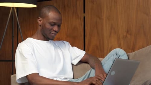 Man Sitting On Couch Using Laptop Indoors