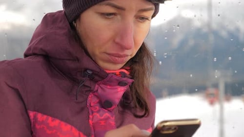 Attractive Young Woman at a Mountain Ski Resort. Standing on a Snow Using on Her Mobile Phone