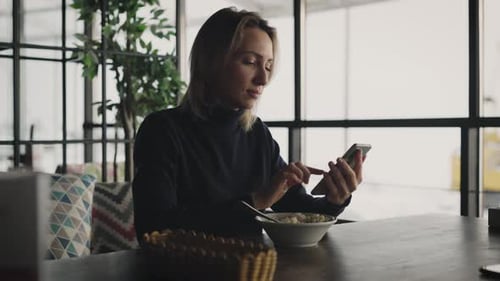 Attractive Blonde Woman Uses a Smartphone in a Cafe