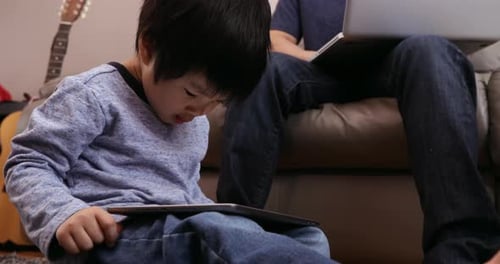 Child Using Tablet with Man on Laptop Indoors