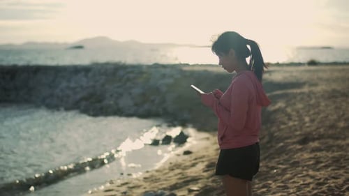 Woman Using Phone on Beach at Sunrise