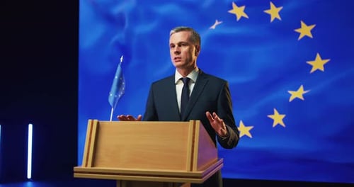 Man Speaking at Podium with EU Flag Backdrop